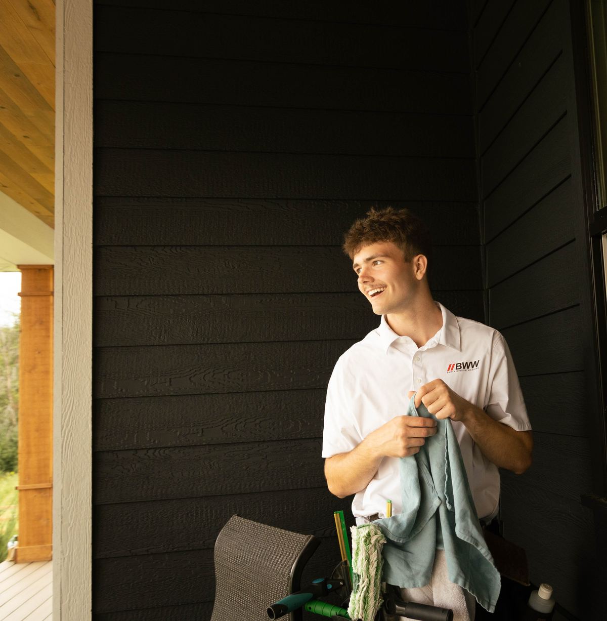 Technician with microfiber cloths in hand on a covered porch, ready to detail the next window