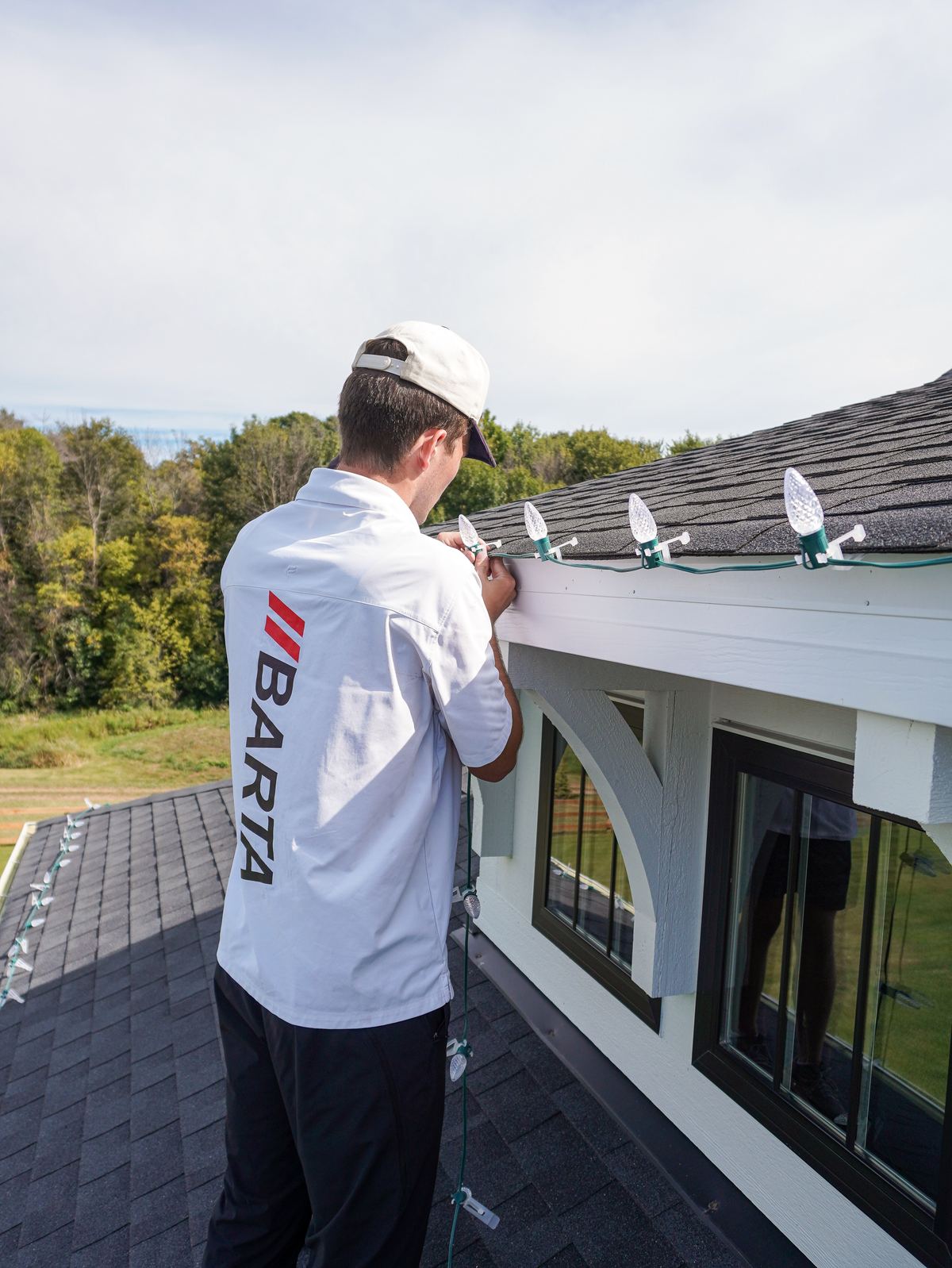 Technician fastening holiday light clips along the roofline of a white home
