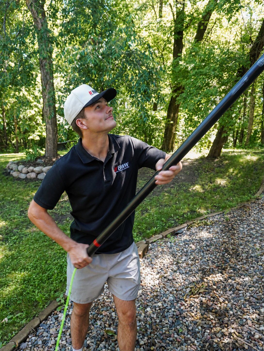 Technician looking up while guiding a water-fed pole brush toward a home's upper windows