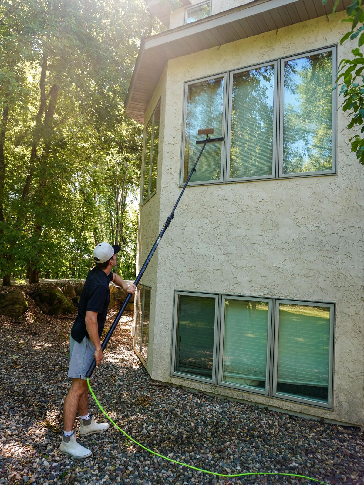 Technician reaching the top windows of a stucco home's corner with a water-fed pole
