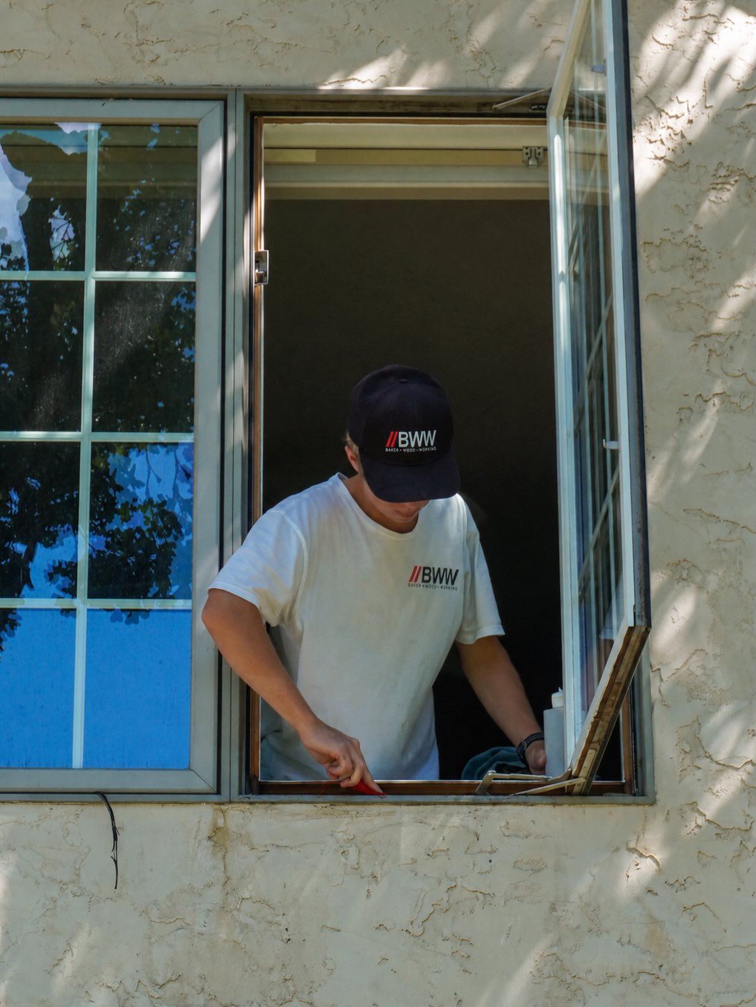 Technician cleaning around an opened window sash from inside the home