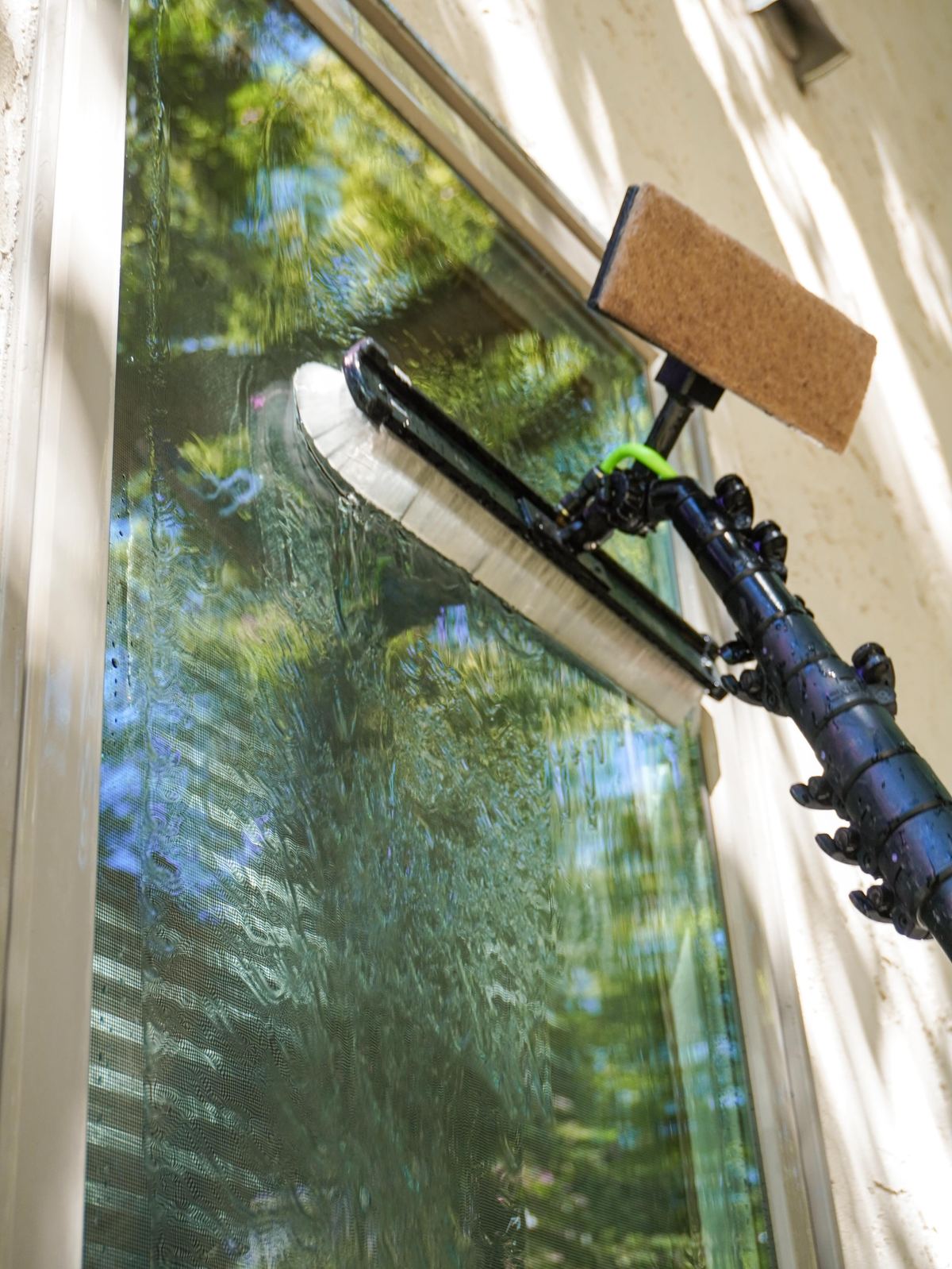 Close-up of a water-fed pole brush head working across leafy reflected glass