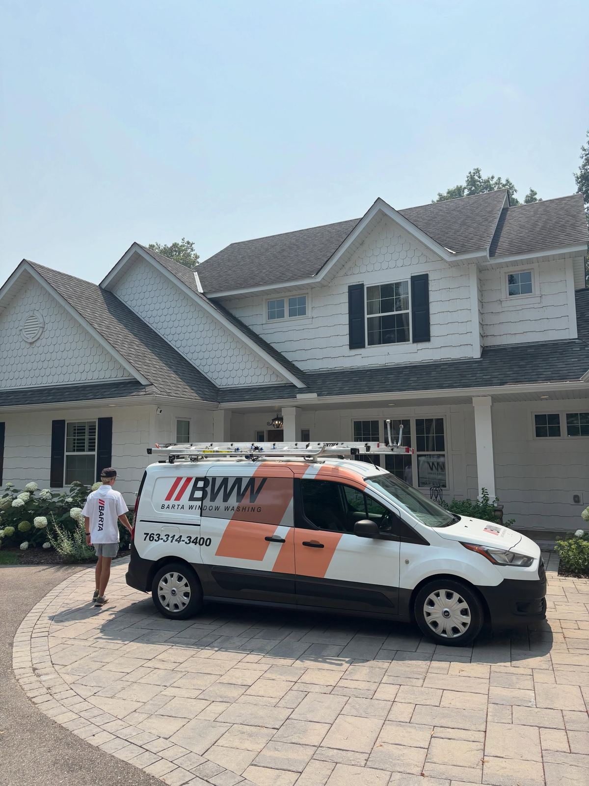 Barta Window Washing van arriving on the paver driveway of a two-story home