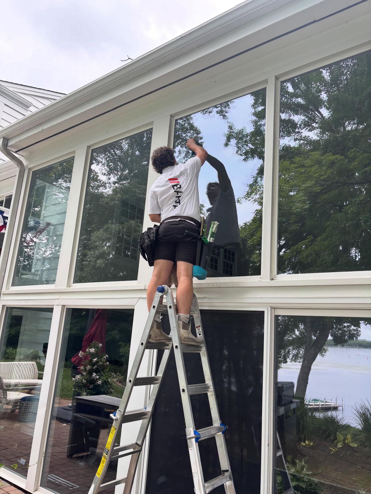 Technician on a ladder cleaning lakeside sunroom windows
