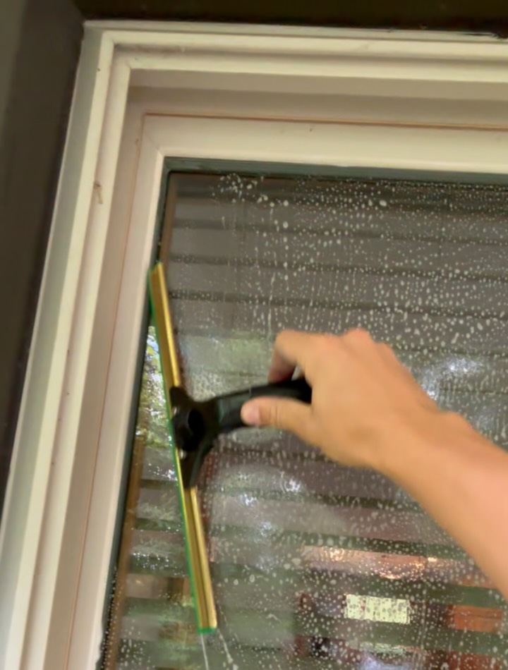 Brass-channel squeegee clearing suds from a textured privacy-glass window