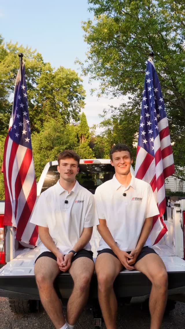 Two Barta Window Washing crew members on a pickup tailgate flanked by American flags
