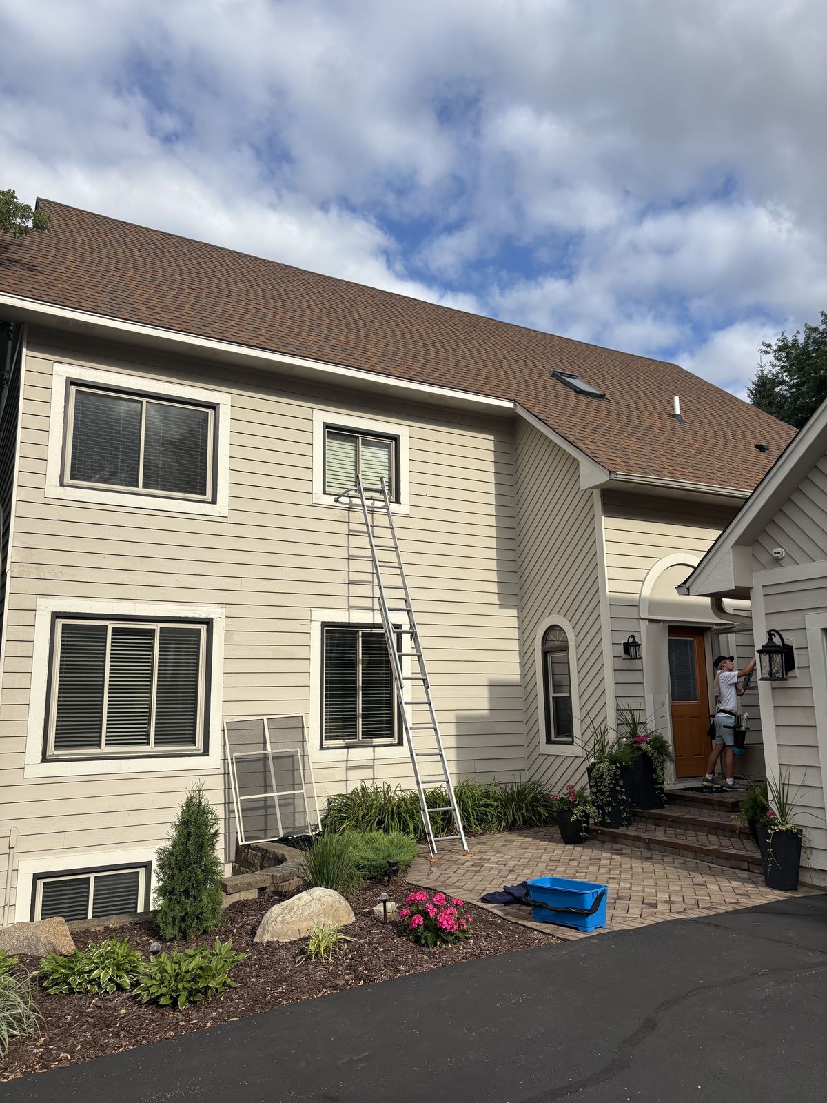 Barta crew member cleaning by the front door of a Chanhassen home, with an extension ladder set against a second-floor window