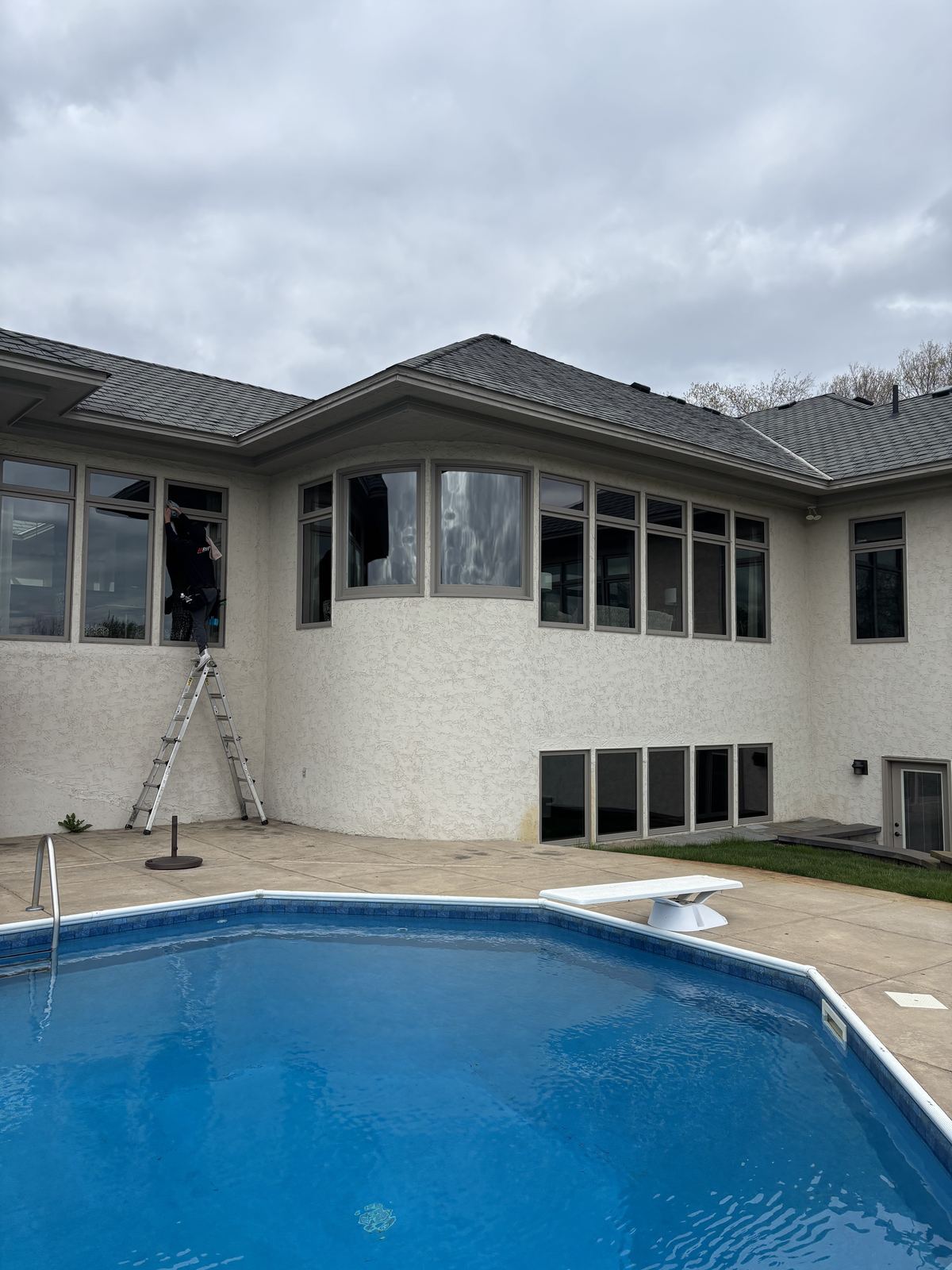 Crew member on a stepladder cleaning the main-floor back windows of a Delano home beside a backyard pool