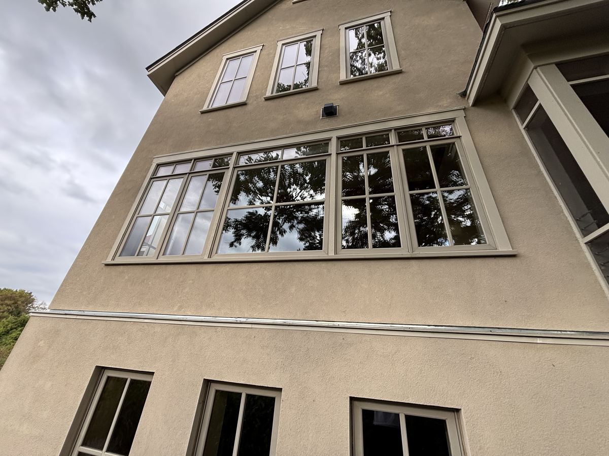 The tall stucco back of a Minnetrista home with a wide band of divided-light windows on the second floor