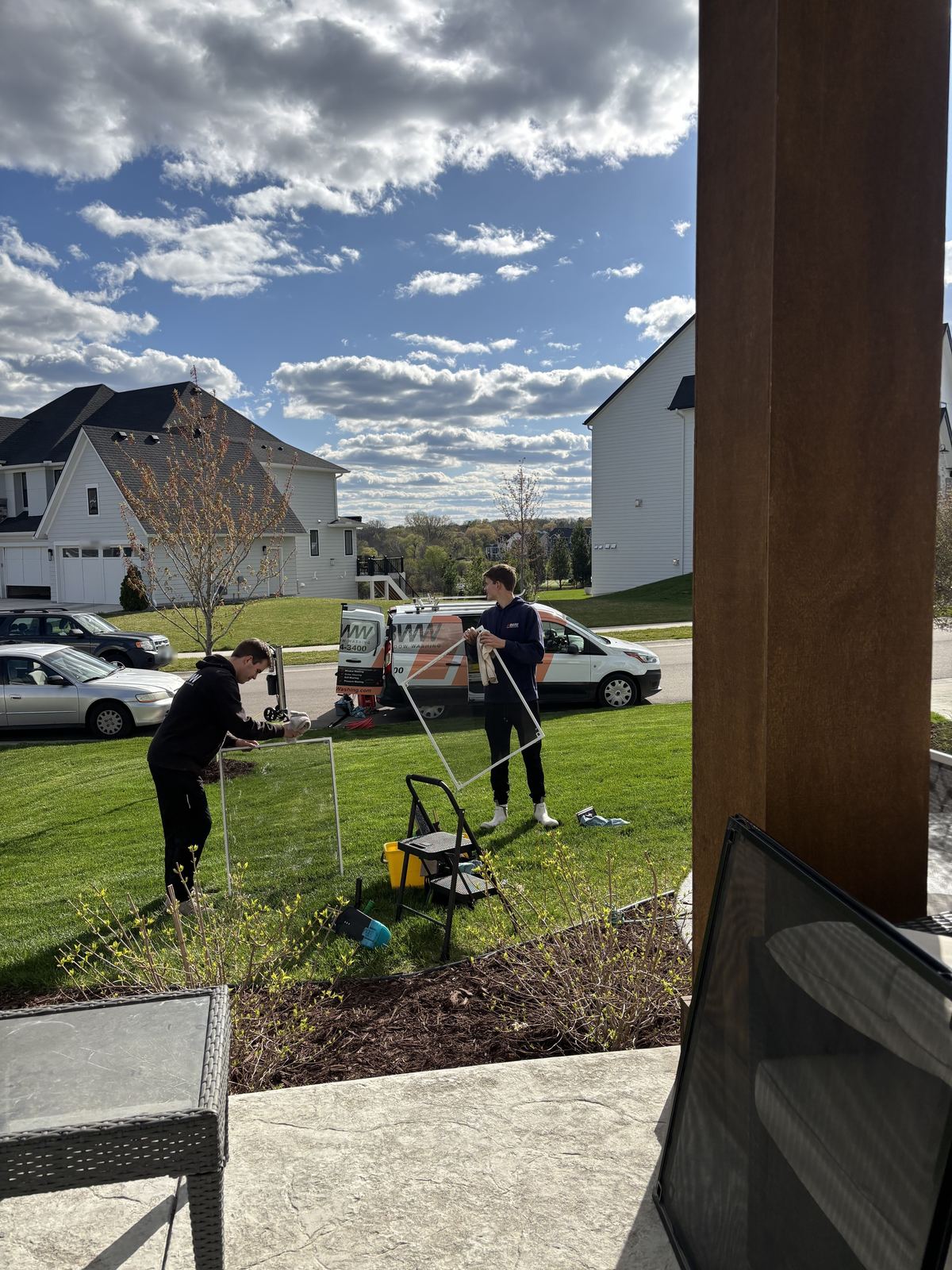 Two Barta technicians hand-washing window screens on the front lawn of a Plymouth home