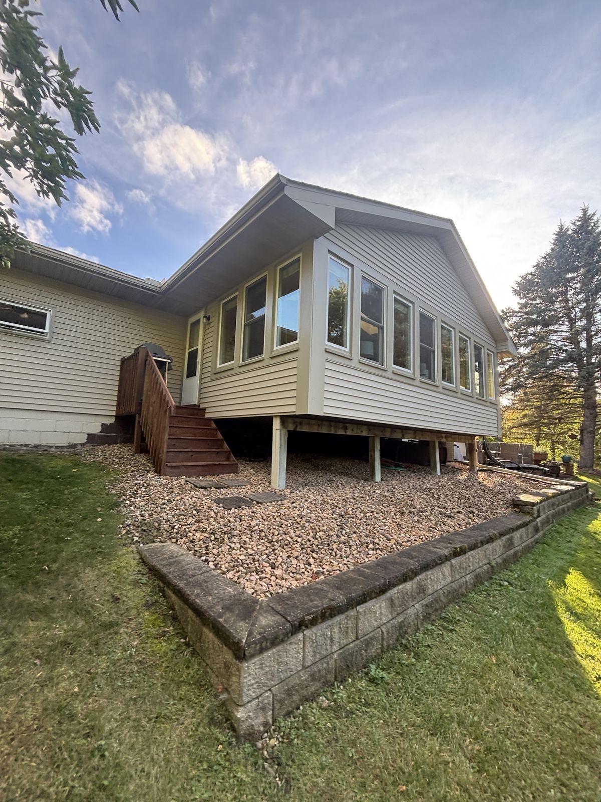 The sunroom on the back of a Victoria home, a long row of windows above a rock bed and block retaining wall