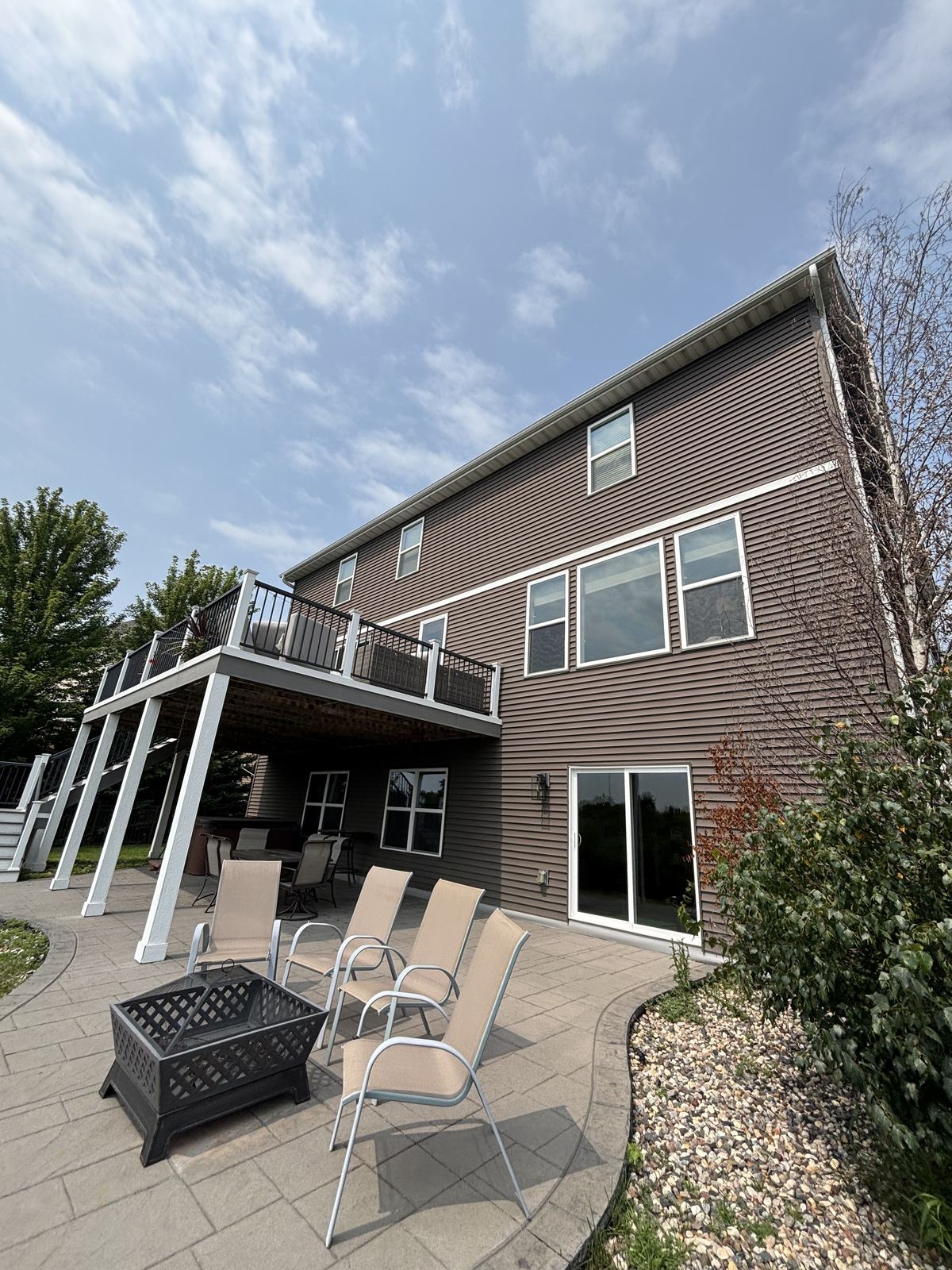 The tall back of a Victoria home, three stories of windows rising above a patio with a deck and fire pit