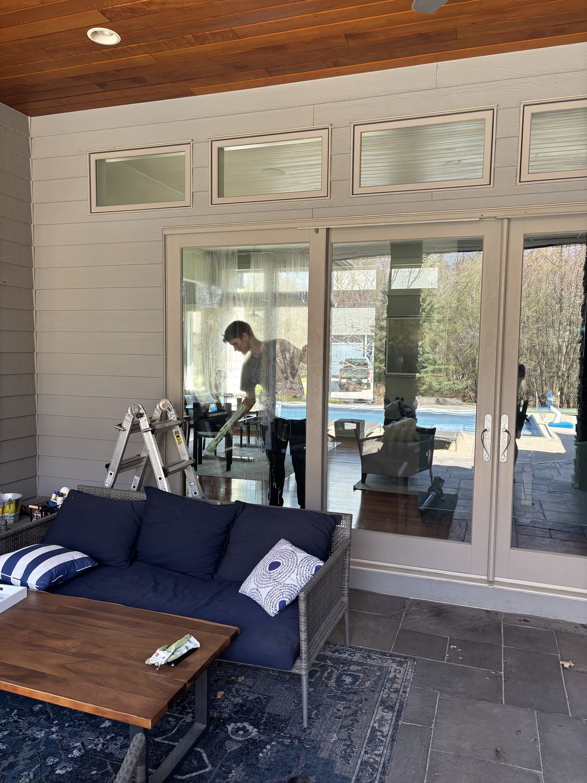 Barta technician cleaning patio doors and transom windows from inside a covered patio at a Waconia home