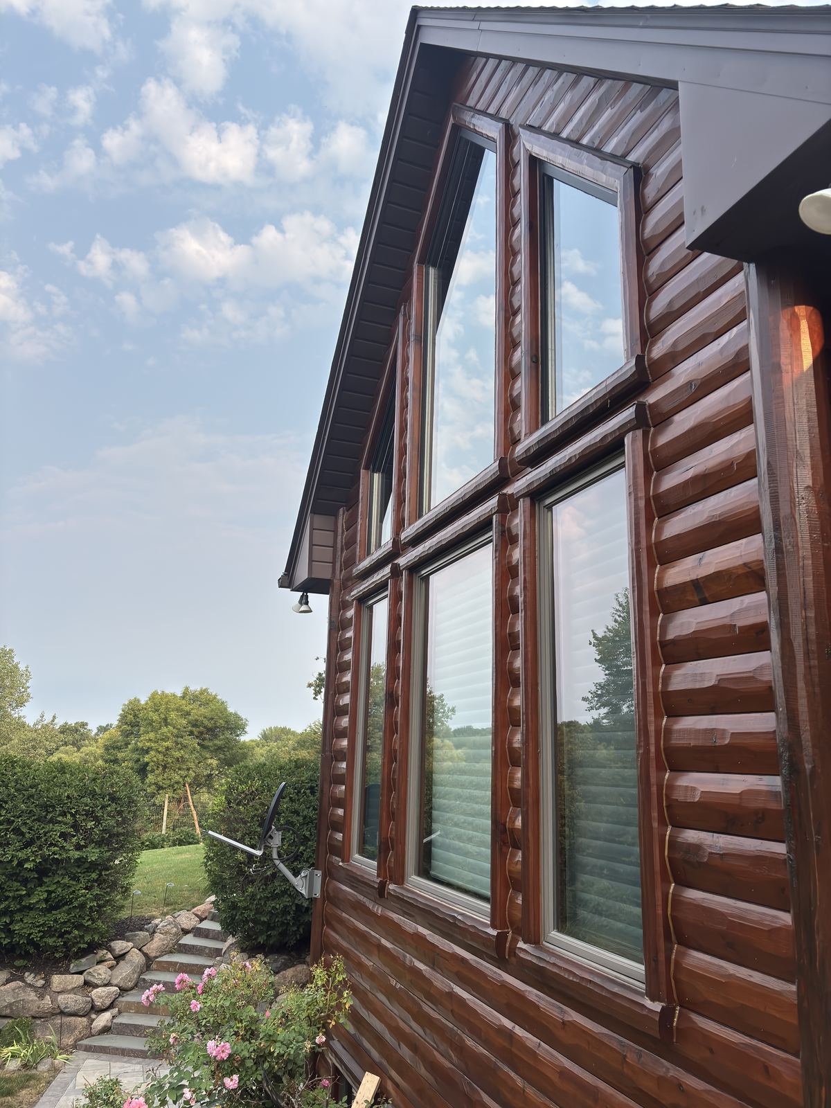Tall windows on the gable end of a log-sided home near Watertown, freshly cleaned and reflecting the sky